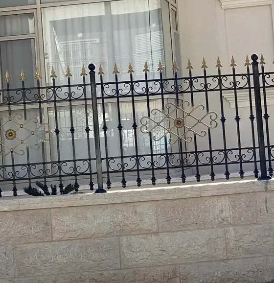 גדר ברזל מעוטרת ביציקות פליז על גבי קיר אבן
